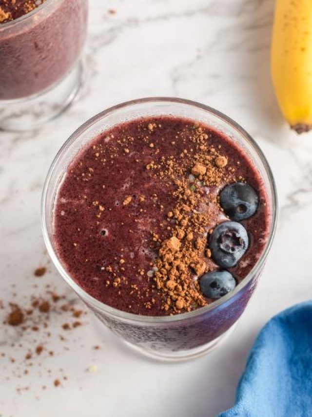 45 degree view of a brown/blue smoothie in a glass with a line of cocoa powder and a line of blueberries on the top