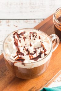 side view of a glass mug with light brown coffee and topped iwth whipped cream and chocoalte sauce