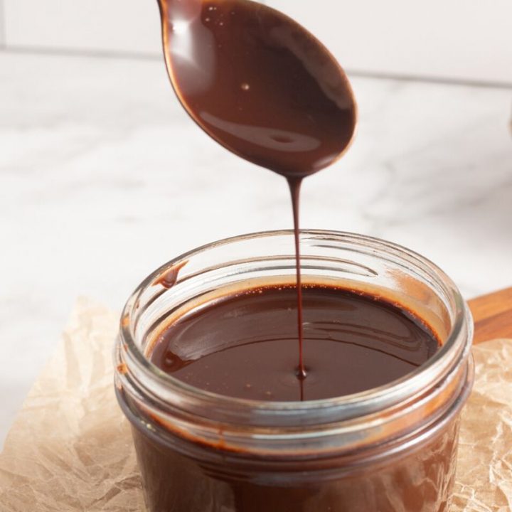 side view of a glass with chocolate sauce and a spoon dripping the sauce