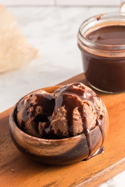side view of a chocolate ice cream in a wooden bowl drizzled in chocolate sauce