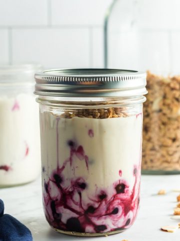side view of a glass mason jar with blueberries on the bottom and yogurt on top