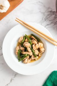 top view of chicken and green beans in a white bowl with chopsticks on the side