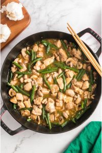 top view of a round skillet with chunks of chicken and green beans in a thick sauce