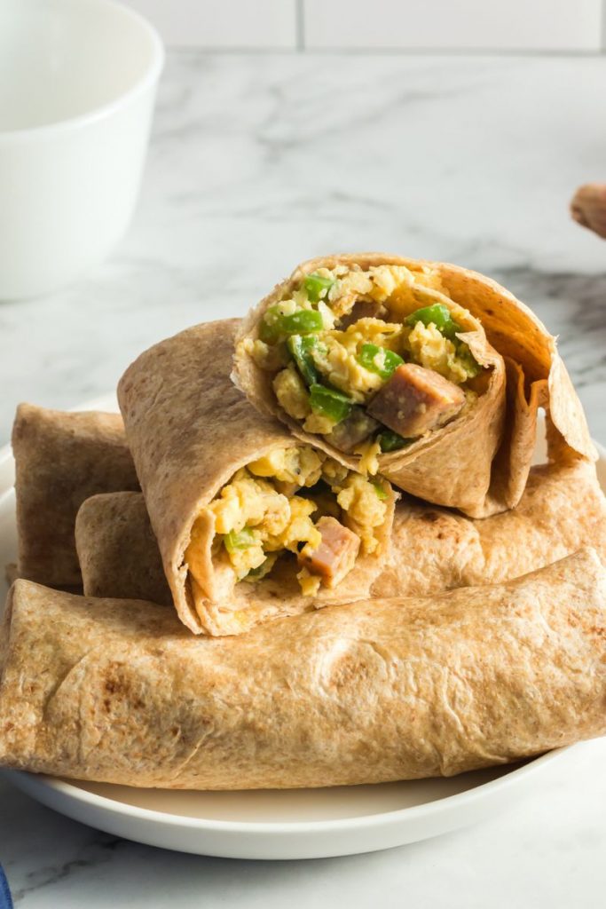 side view of a breakfast burrito cut in half and showing the eggs, green bell peppers and tortilla
