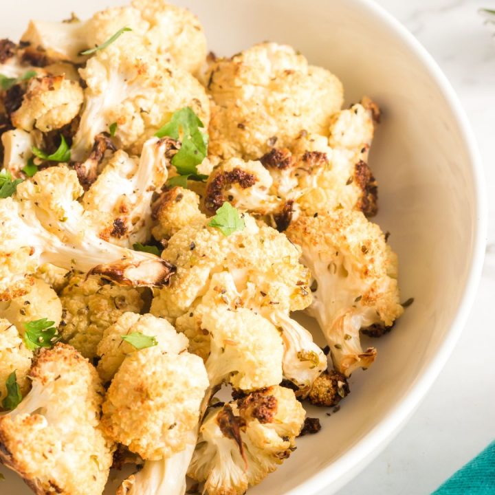 white bowl with roasted cauliflower in it and a green garnish