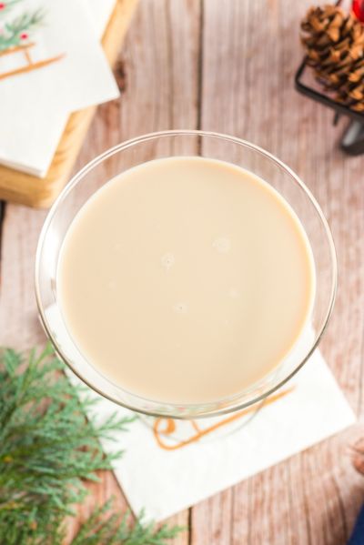 top view of a martini glass iwth brown milky cocktail. There is a pine tree branch and a christmas napkin