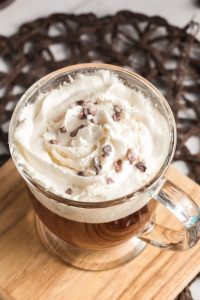 side view of a glass mug with coffee and topped with whipped cream and cocoa nibs