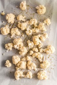 top view of cauliflower florets sprinkled with oil and oregano on a sheet pan with parchment paper