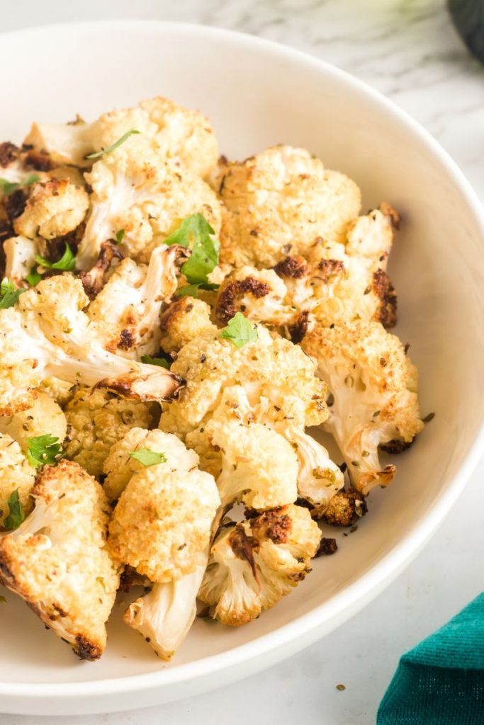 white bowl with roasted cauliflower in it and a green garnish