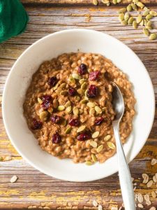 top view of a white bowl with cooked oatmeal topped with cranberries and pumpkin seeds