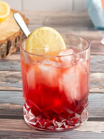 side view of a red mocktail in a glass cup garnished with a slice of lemon