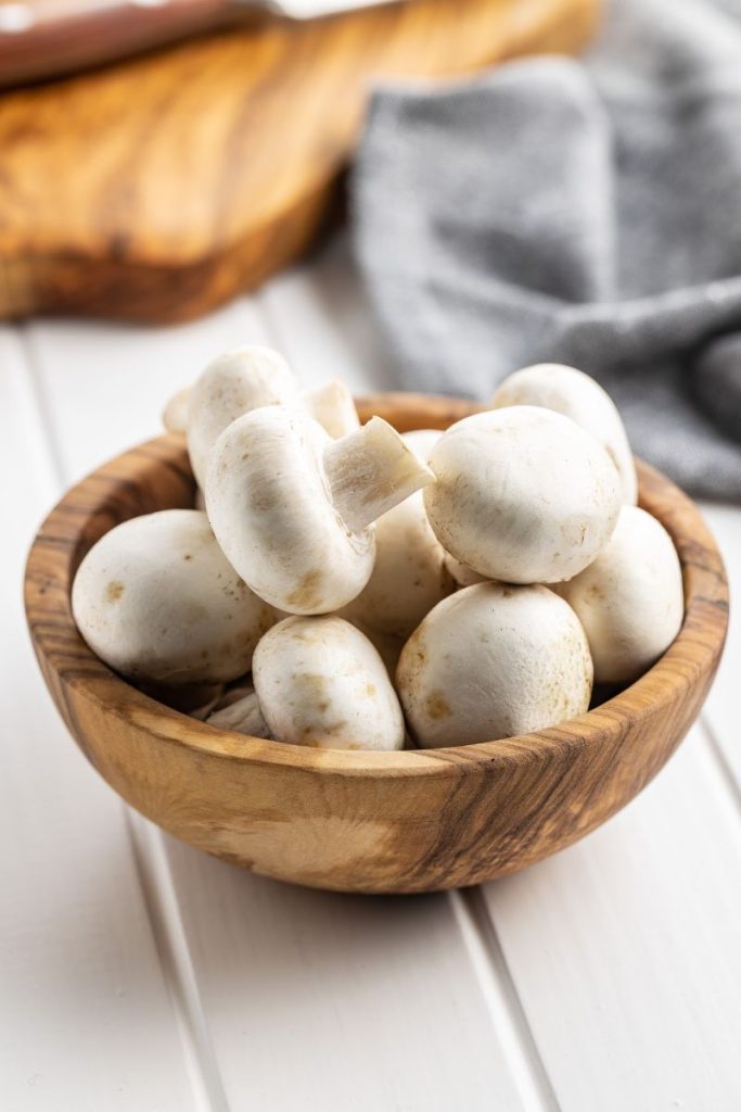 a wooden bowl with white raw mushrooms