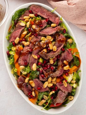 top view of greens with toasted peanuts, sliced steak and carrots